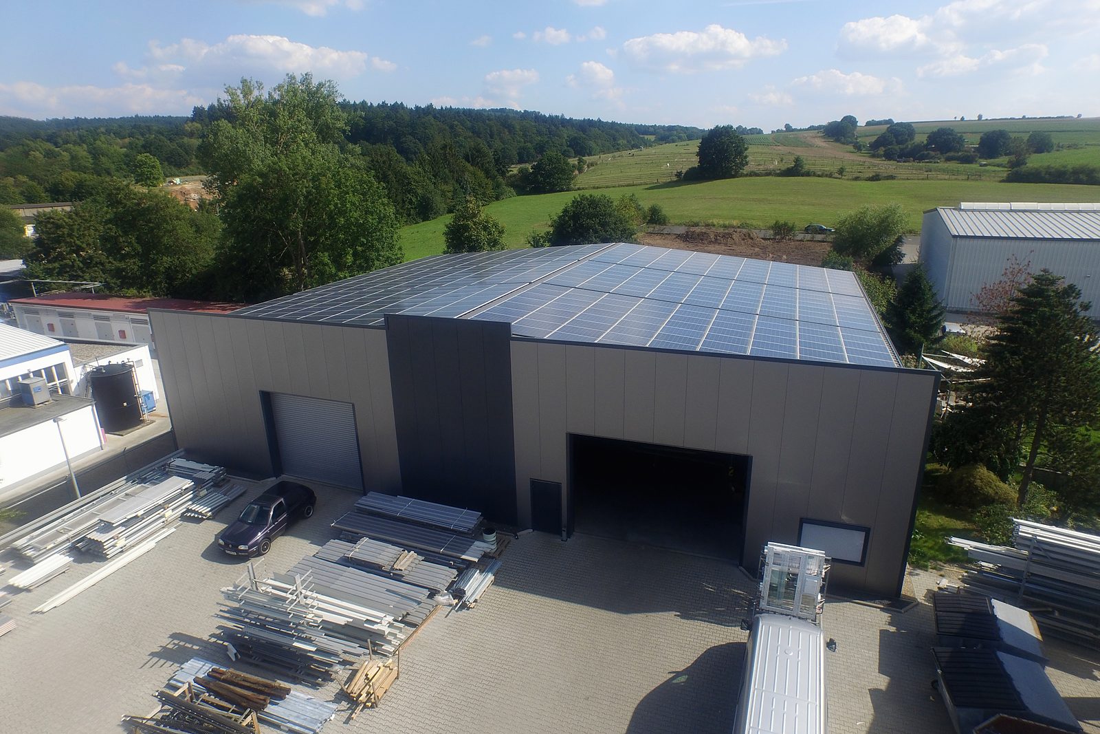 Luftbild der Halle von Bergheimer Stahlhallen mit Solardach, davor gelagerte Stahlteile