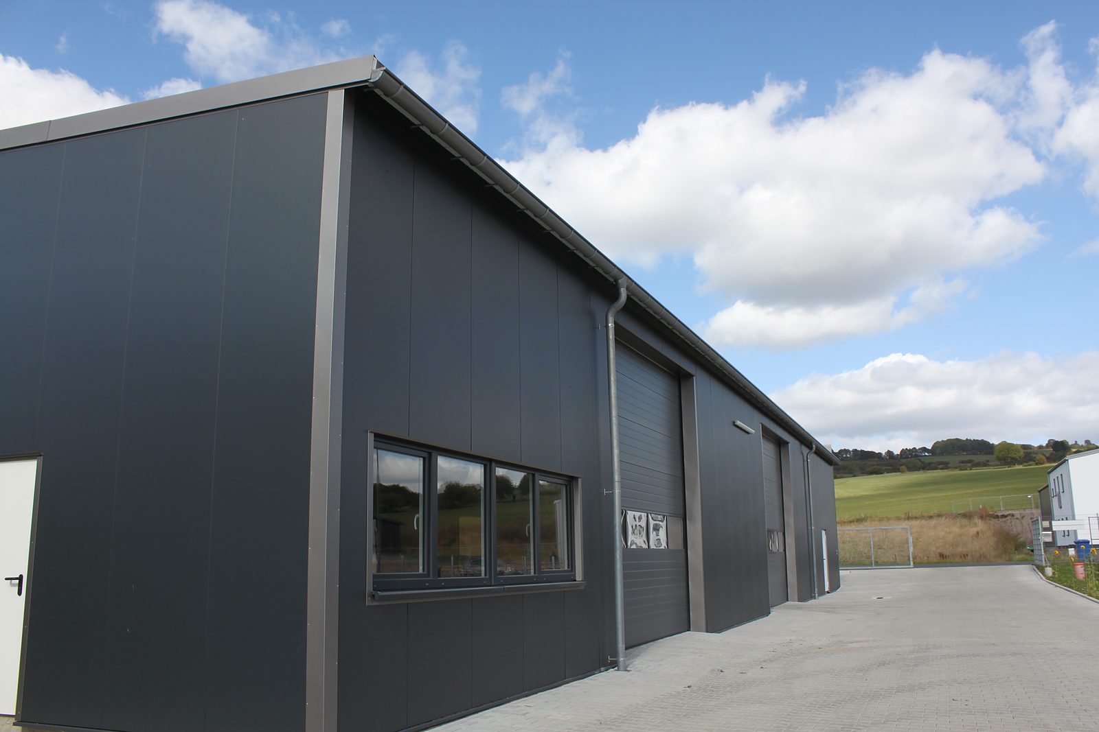 Dunkle Lager- und Logistikhalle aus Stahl mit Fensterband und Sektionaltoren unter Wolkenhimmel, gebaut von Bergheimer Stahlhallen in Schlüchtern